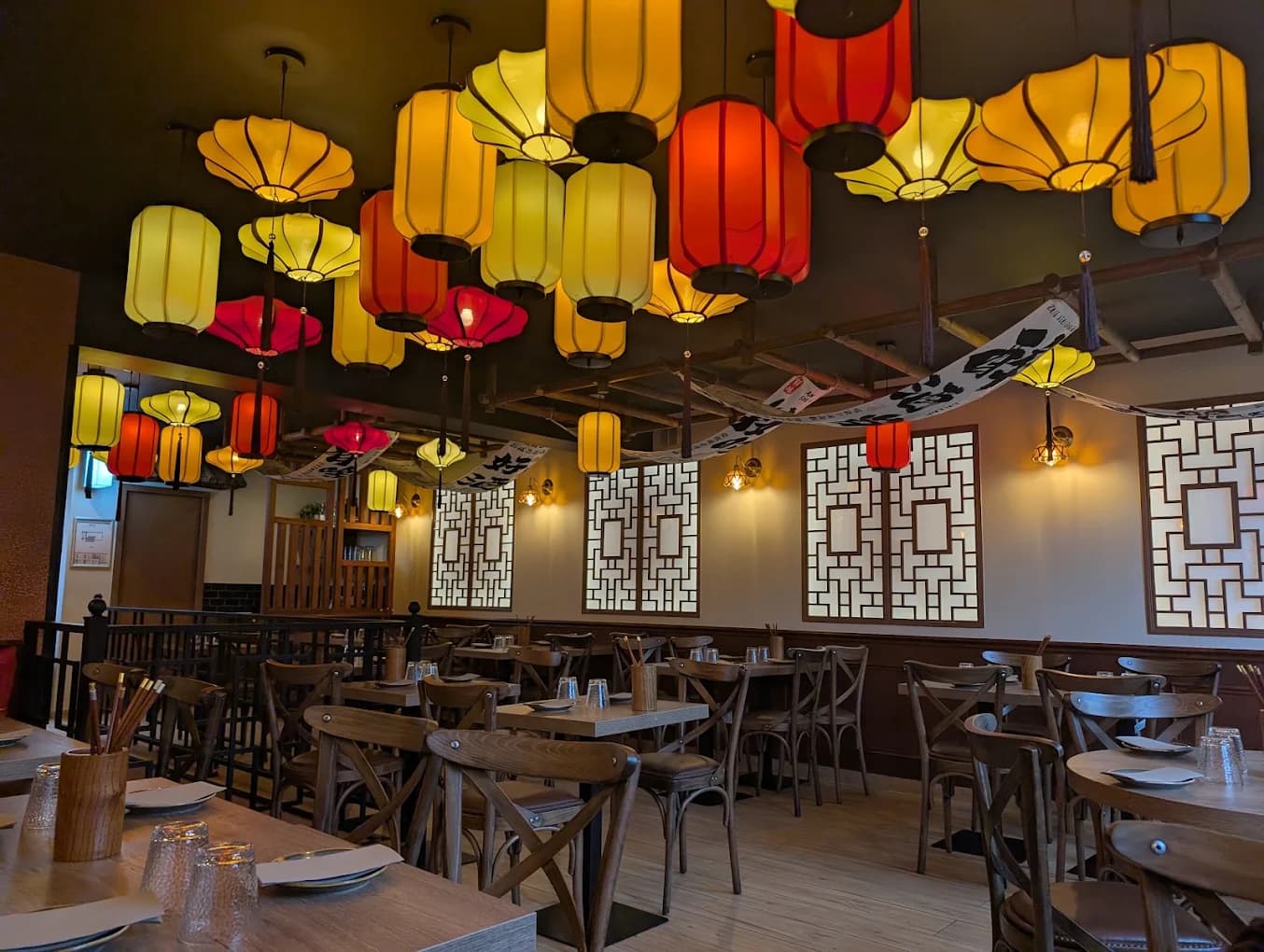 Salle de Bao City : plafond de lanternes jaunes et rouges, panneaux à claustras et tables dressées.